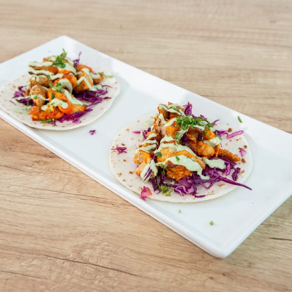 Two chicken tacos with red cabbage and green sauce on a white rectangular plate.