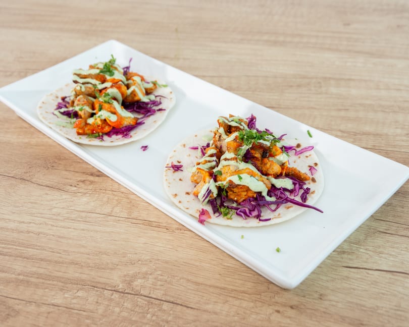 Two chicken tacos with red cabbage and green sauce on a white rectangular plate.