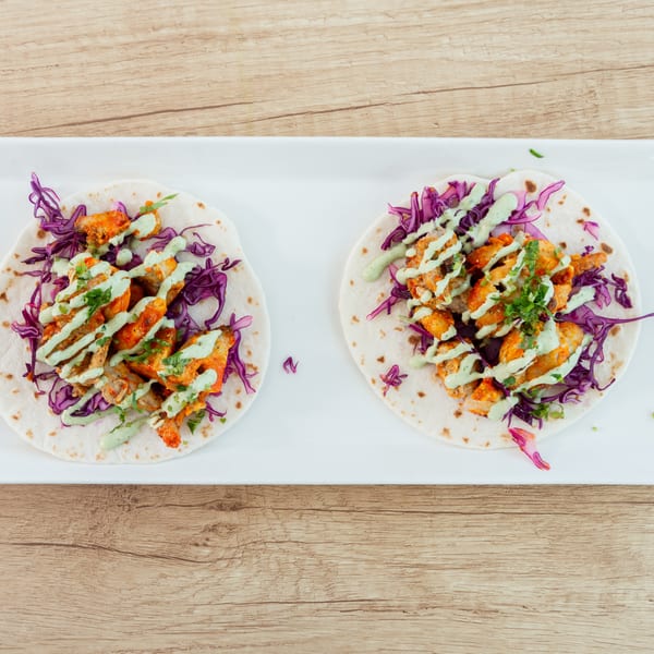 Two chicken tacos with red cabbage and green sauce on a white rectangular plate.