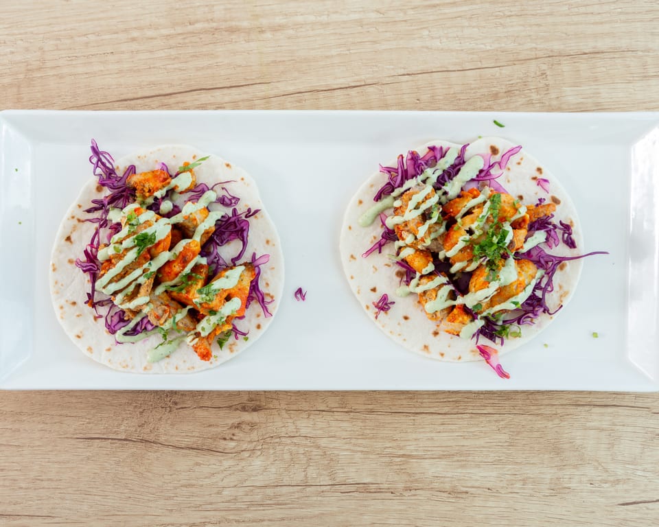 Two chicken tacos with red cabbage and green sauce on a white rectangular plate.