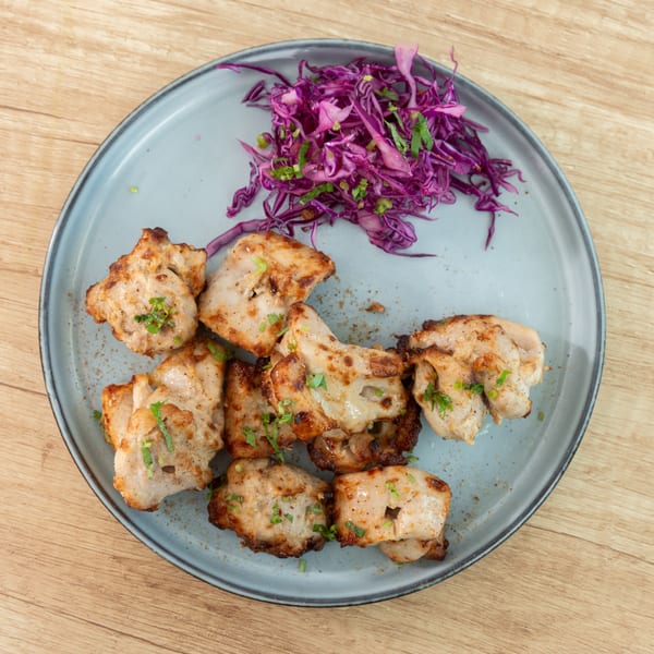 Grilled chicken pieces with fresh herbs and a side of shredded purple cabbage on a blue plate.