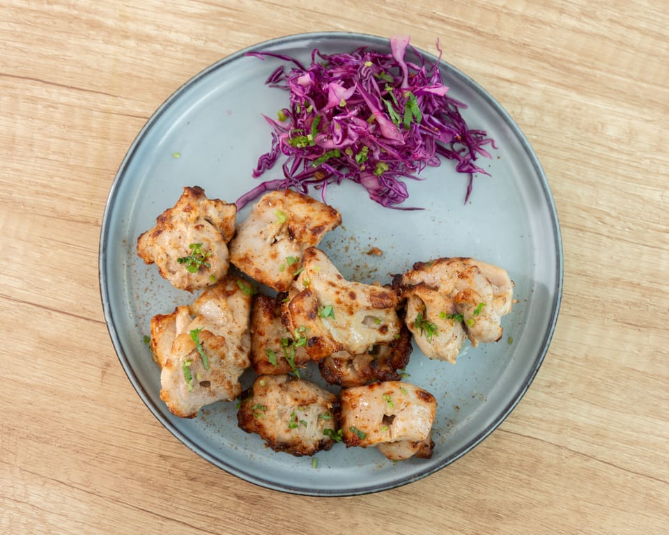 Grilled chicken pieces with fresh herbs and a side of shredded purple cabbage on a blue plate.