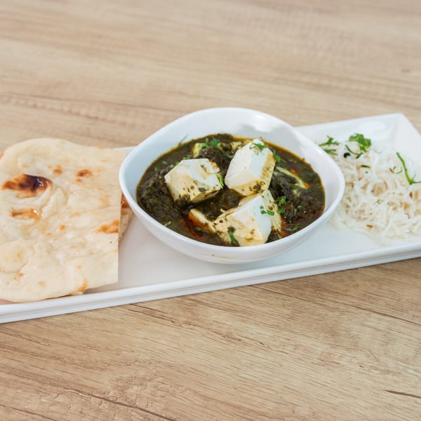 Palak Paneer with naan and rice, served on a white rectangular plate on a wooden table.