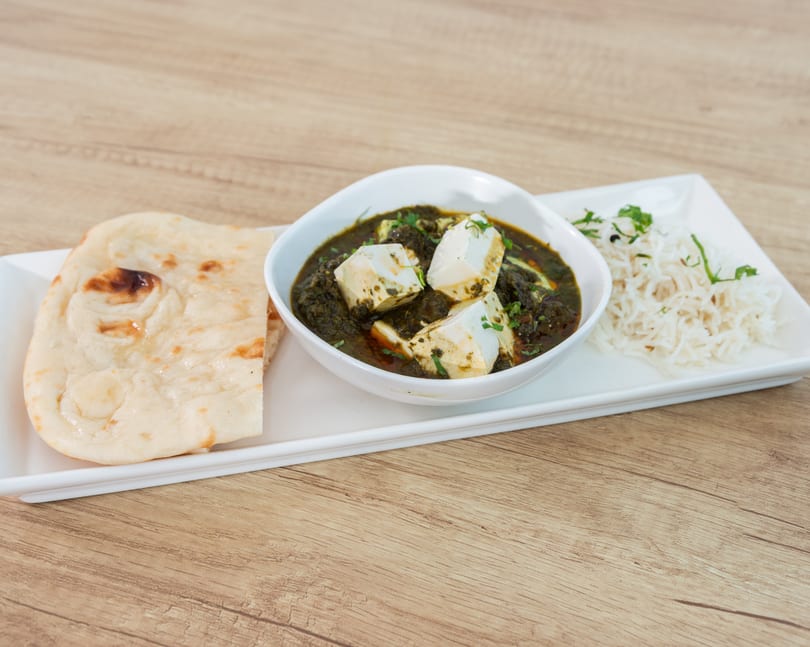 Palak Paneer with naan and rice, served on a white rectangular plate on a wooden table.