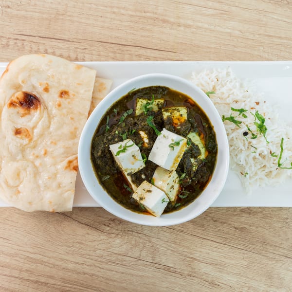 Palak Paneer with rice and naan bread on a white rectangular plate, on a wooden table.