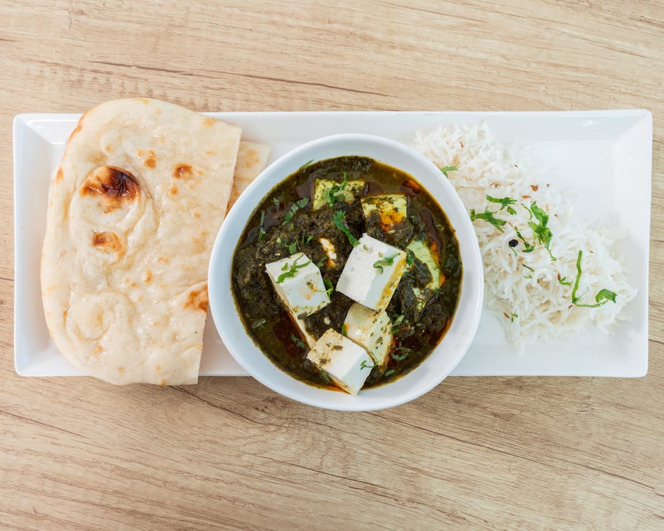 Palak Paneer with rice and naan bread on a white rectangular plate, on a wooden table.