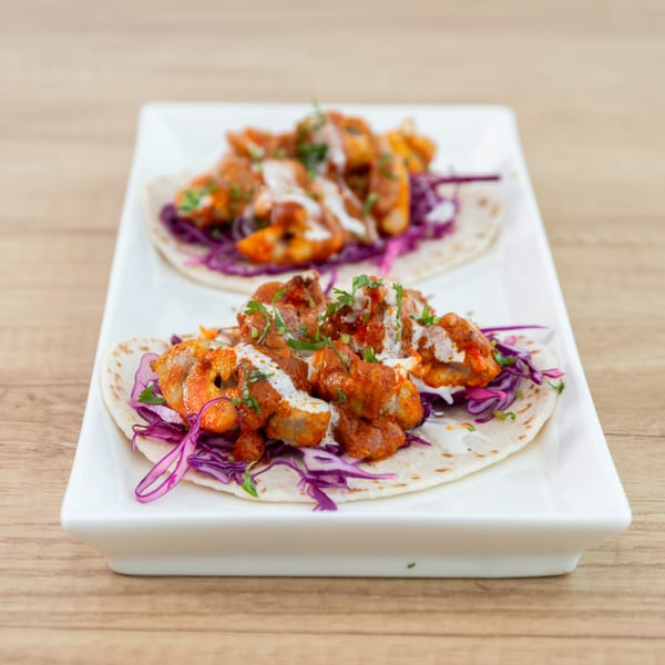 Two chicken tikka tacos with red cabbage, white sauce, and cilantro on a white rectangular plate.