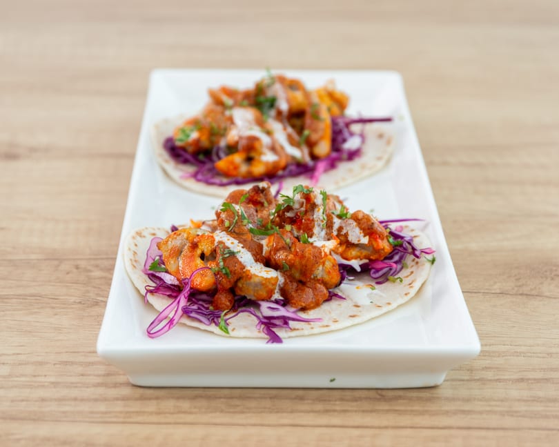Two chicken tikka tacos with red cabbage, white sauce, and cilantro on a white rectangular plate.