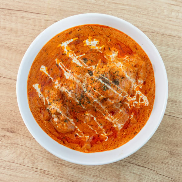 Overhead view of a white bowl filled with orange butter chicken, drizzled with cream and herbs.