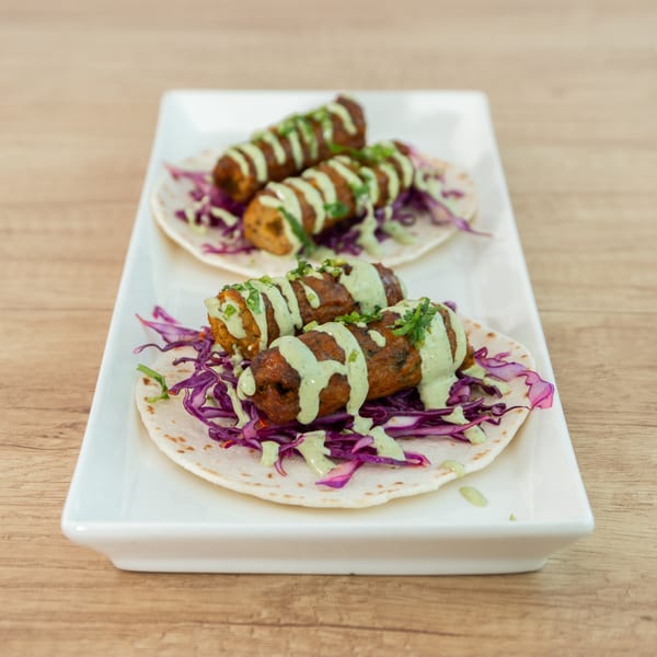Three kebabs on tortillas with red cabbage and green sauce, served on a white rectangular plate.