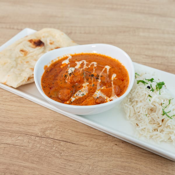 A bowl of butter chicken with naan bread and rice on a white rectangular plate.