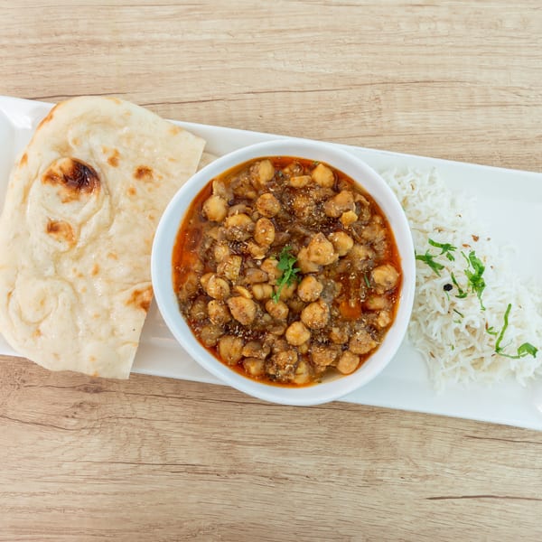 Chana masala with naan bread and basmati rice, garnished with fresh cilantro, on a white plate.