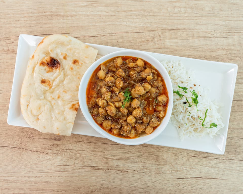 Chana masala with naan bread and basmati rice, garnished with fresh cilantro, on a white plate.